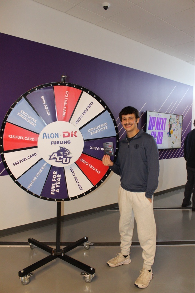 Freshman holding fuel gift card in front of the ACU/DK prize wheel.
