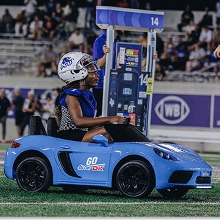ACU athlete driving a mini car branded 'Go Alon/DK' on the field